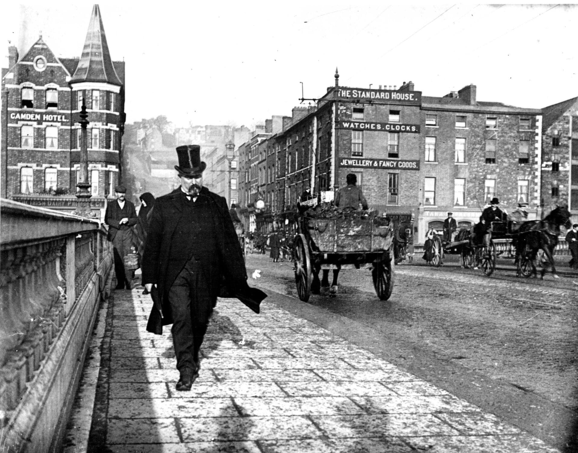 Old black and white photograph of man in tall hat crossing Patrick's Bridge in Cork