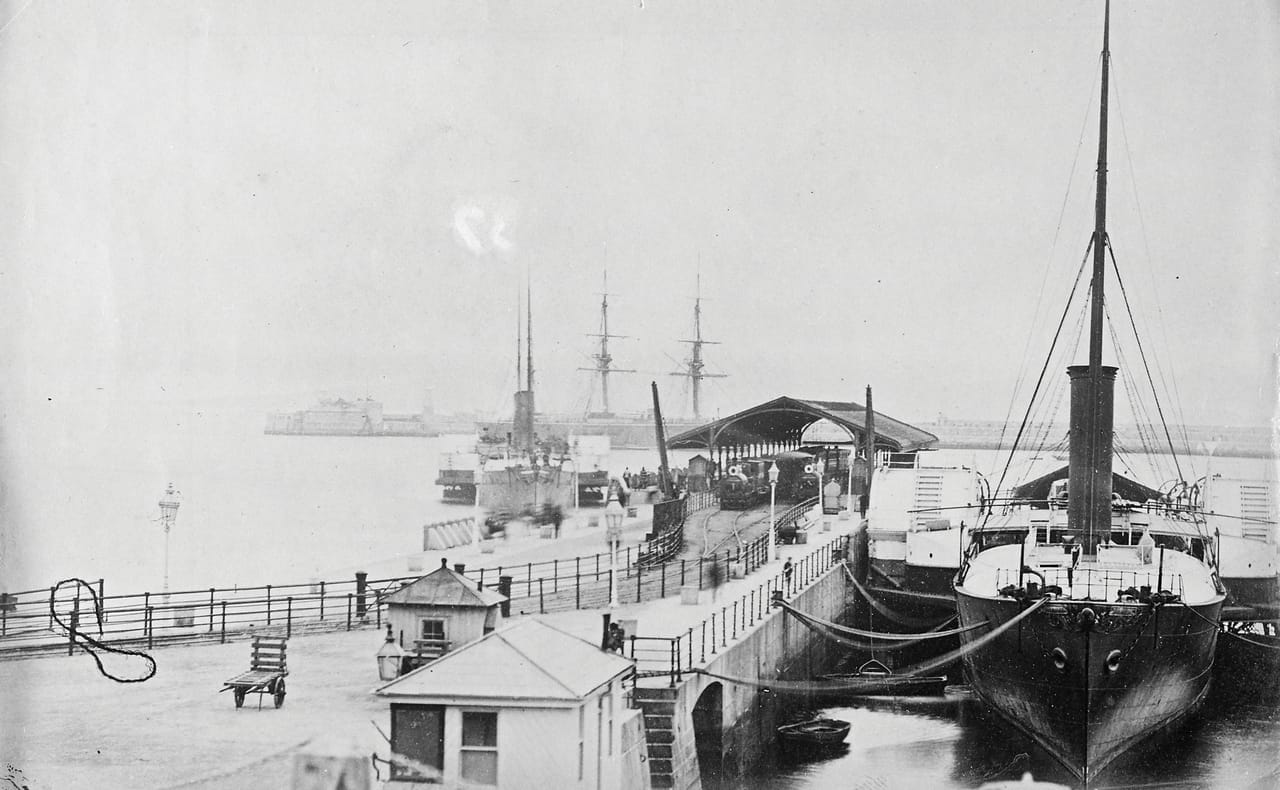 Black and white photograph taken in about 1890 showing ships moored at the Carlisle Pier in what was then called Kingston Harbour, and is now Dun Laoghaire Harbour. The photograph is from the Clarke Photographic Collection in the National Library of Ireland.